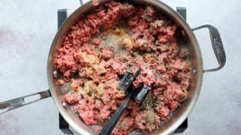 pink ground beef cooking in a skillet with a ground beef masher in the skillet