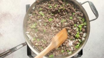 stirring a skillet with cooked ground beef, bell peppers and onions