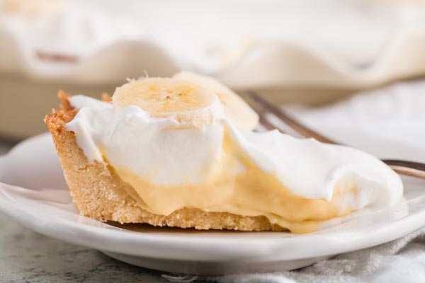 slice of keto banana cream pie on a white plate with a thick crust