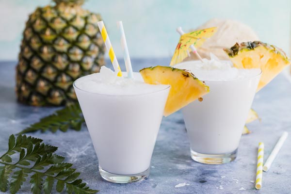 two pina colada cocktails with pineapple wedges and straws