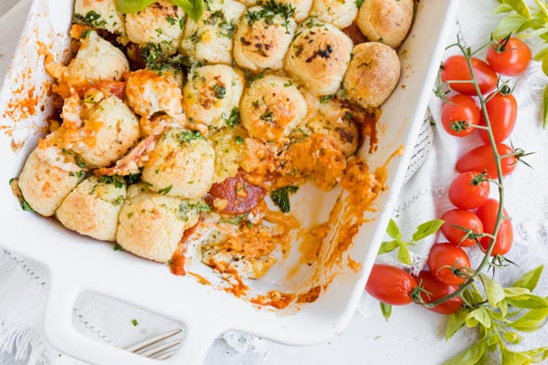 pizza casserole with a serving taken out next to tomatoes and basil