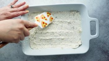 a white cheese mixture spread into a dish with a pizza spatula
