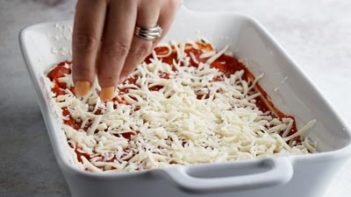 sprinkling shredded mozzarella cheese in a baking dish