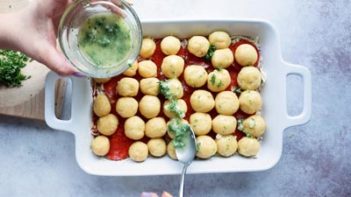 spooning butter and parsley mixture on bread rolls in a casserole dish