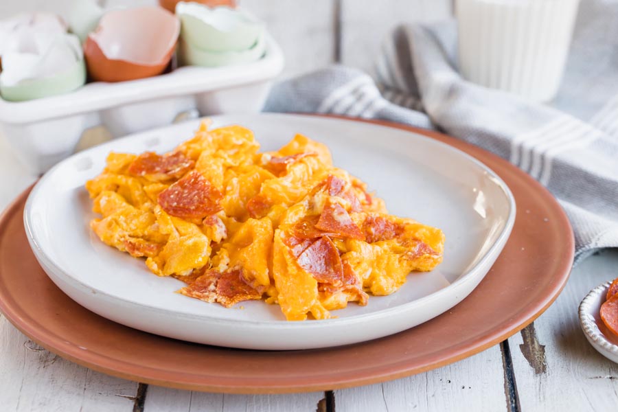 sliced pepperoni and egg scrambled on a white plate with a glass of milk behind