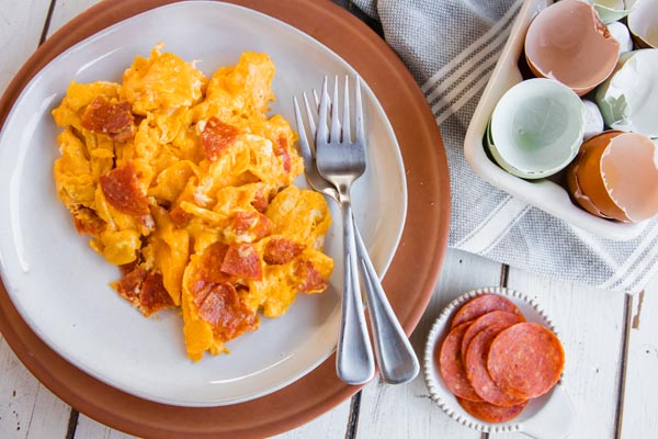 a plateful of pepperoni scrambledeggs with forks and slices of pepperoni next to it