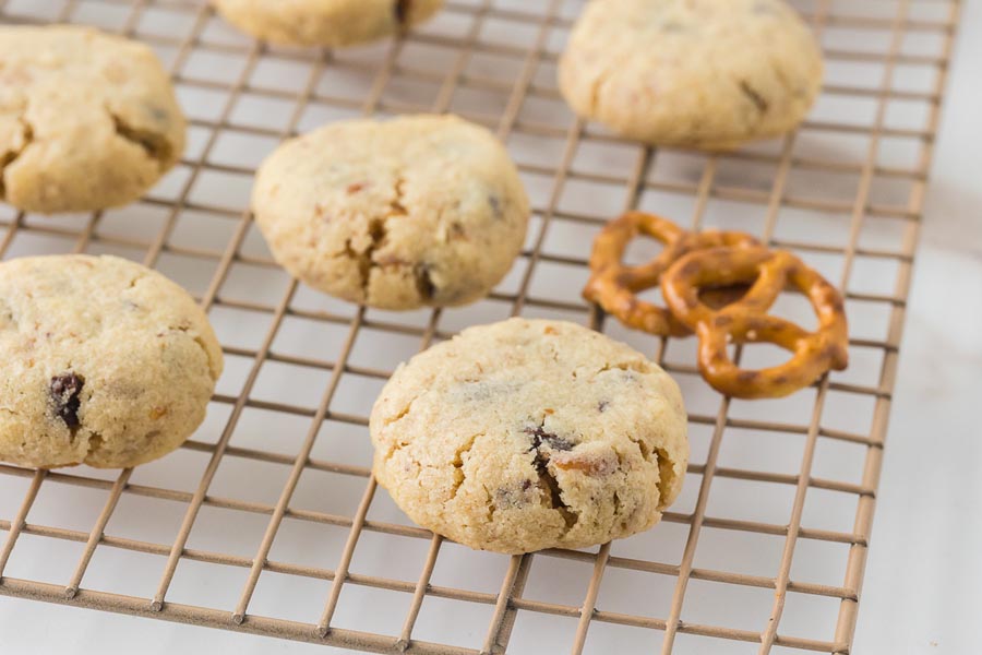 Keto pretzel chocolate chip cookies resting on a wire cooling rack with pretzels placed nearby for garnish.