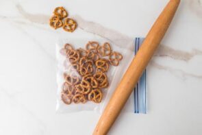 Rolling pin beside a zip-top bag of mini pretzels on a marble surface.