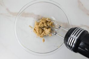 A hand mixer blends the keto cookie dough ingredients into a thick, creamy mixture.