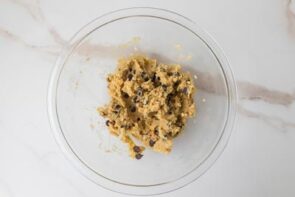 Cookie dough with chocolate chips and golden pieces in a glass bowl.