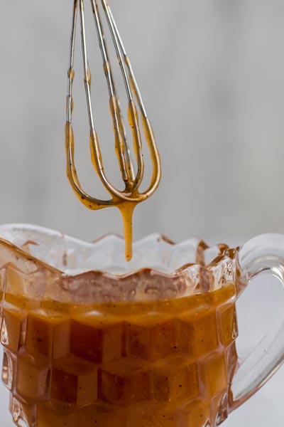 a small jar with caramel syrup and a small whisk dripping syrup from above