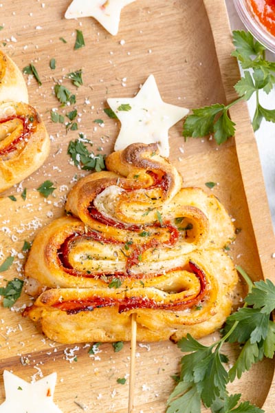 A Christmas tree formed by keto puff pastry and filled with pizza toppings. Chopped parsley lies nearby.