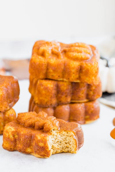 A stack of mini pumpkin bread loaves behind a loaf with a bite taken out of it.