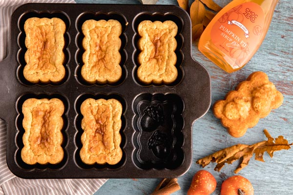 pumpkin bread sitting in a loaf pan with pumpkin syrup next to it