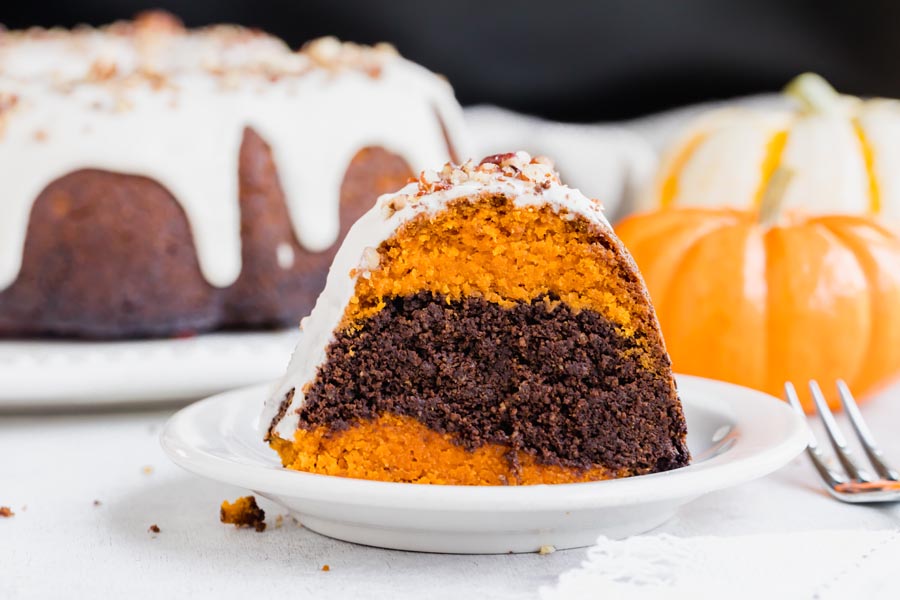 slice of pumpkin and chocolate pumpkin cake on a small plate with a pumpkin in the background and a full bundt cake behind