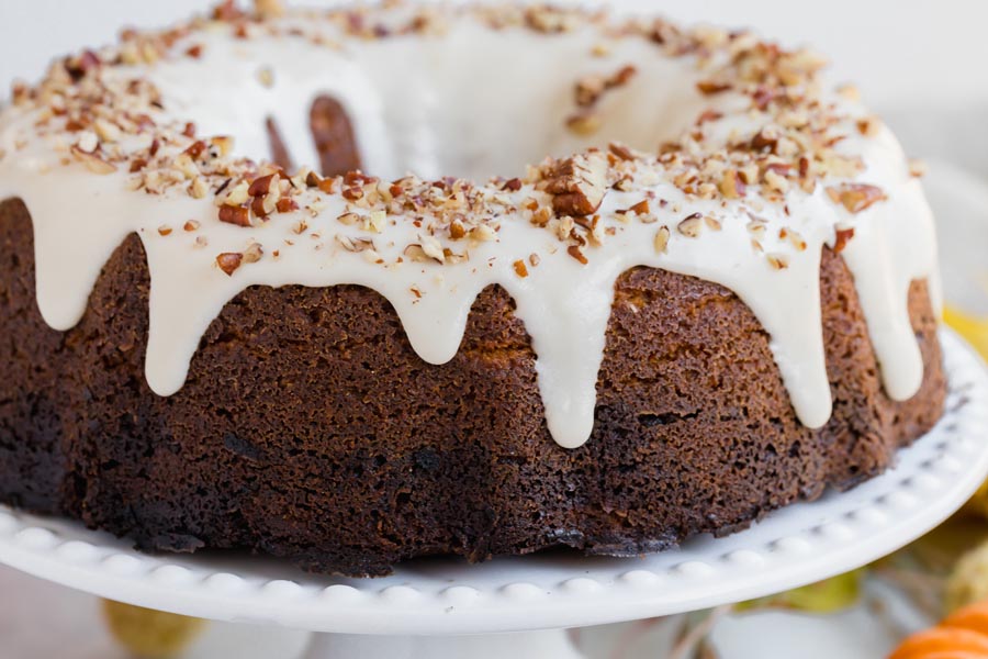 white icing dripping down a bundt cake and topped with nuts