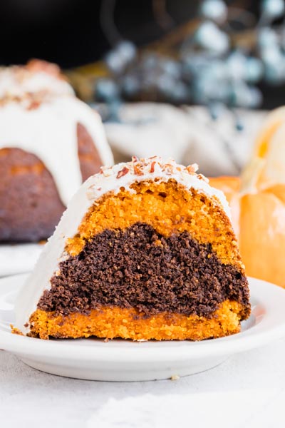 close up of a marbled pumpkin and chocolate bundt cake topped with white icing