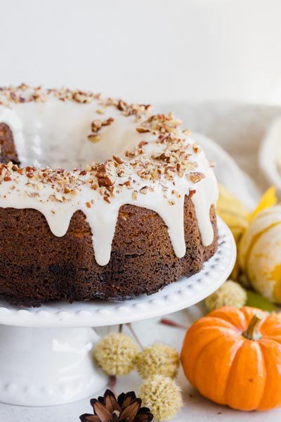 a bundt cake on a white cake stand with icing dripping down and nuts sprinkled all over