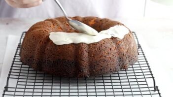 spooning white cream cheese icing on the top of the bundt cake and pushing it along and down