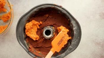 spreading pumpkin cake batter on top of a layer of chocolate cake in a bundt cake