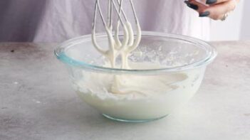 pulling an electric mixer out of icing to show the thin consistency it needs to be