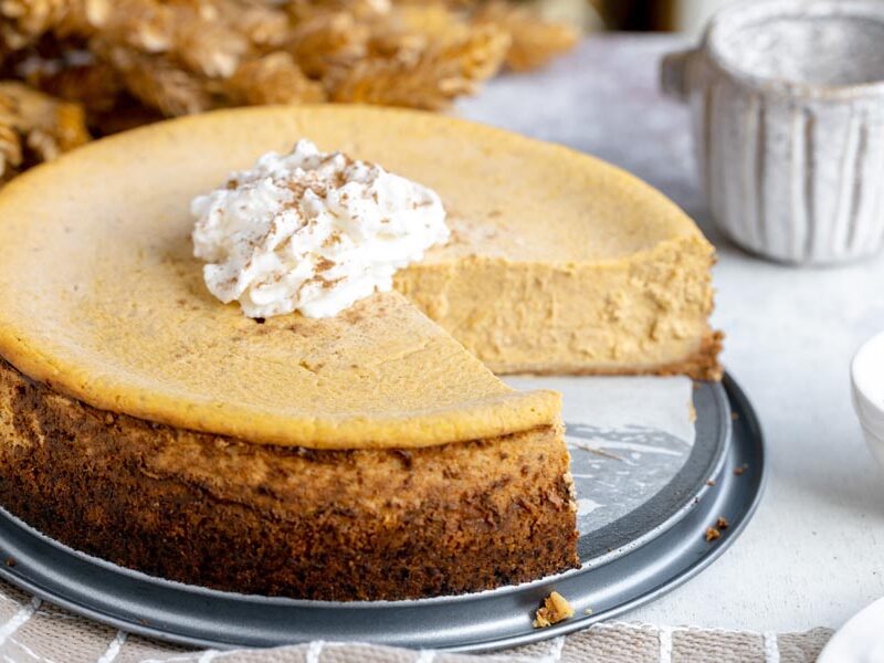 A full keto pumpkin cheesecake with one slice removed and a dollop of whipped cream in the center.