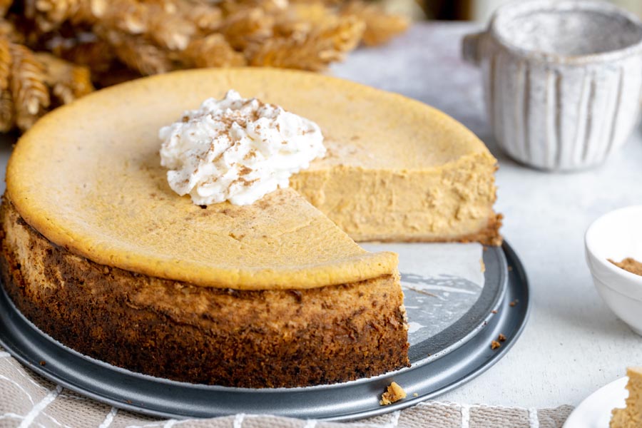 A full keto pumpkin cheesecake with one slice removed and a dollop of whipped cream in the center.