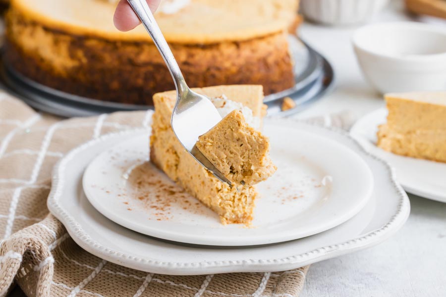 A fork lifting a bite from a creamy slice of keto pumpkin cheesecake with whipped cream.