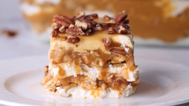 A close-up of a single slice of pumpkin cheesecake lasagna topped with chopped pecans and drizzled with caramel sauce.