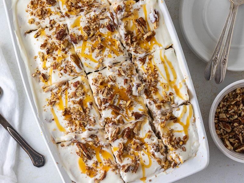 Sliced pumpkin cheesecake lasagna topped with whipped cream, pecans and caramel drizzle.