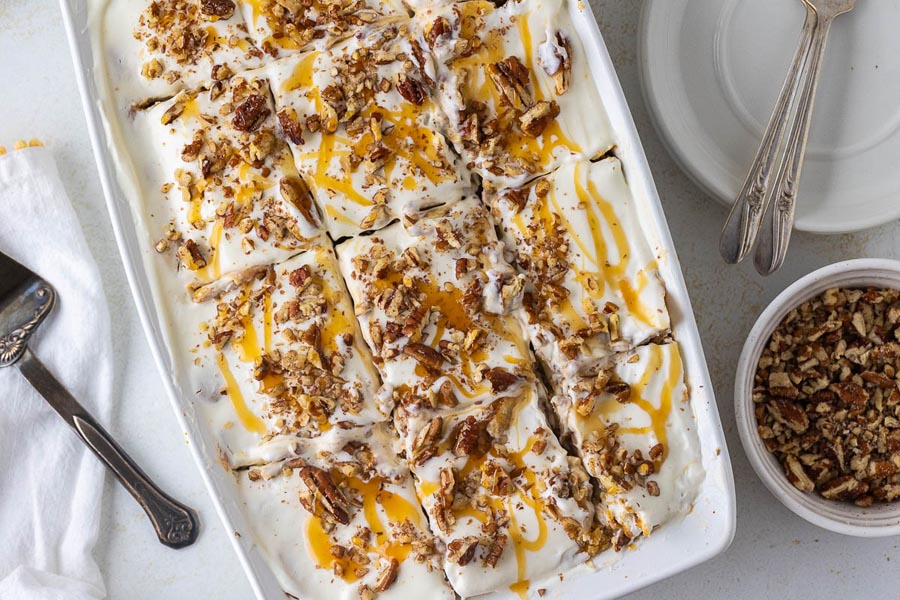 Overhead view of a full pan of pumpkin cheesecake lasagna, sliced and topped with whipped cream, chopped pecans, and caramel drizzle.