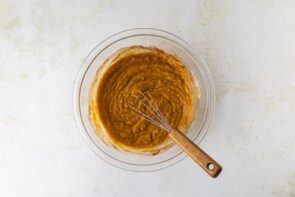 A glass bowl filled with spiced pumpkin cheesecake filling being whisked until smooth.