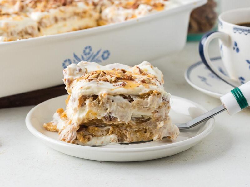 A slice of creamy pumpkin cheesecake lasagna on a white plate with visible layers of pumpkin filling, whipped topping, and pecans.
