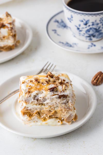 A slice of pumpkin cheesecake lasagna on a plate next to a cup of black coffee in a blue floral teacup.