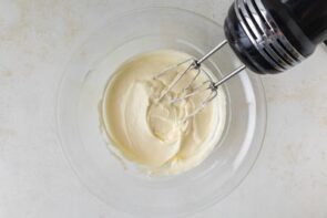 A bowl of whipped cream cheese mixture with an electric hand mixer, ready for layering.