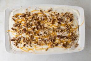 Final assembled pumpkin cheesecake lasagna topped with whipped cream, chopped pecans, and caramel drizzle before slicing.