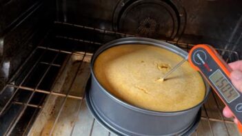 A digital thermometer inserted into the center of a baked pumpkin cheesecake in the oven reading 150.4°F.