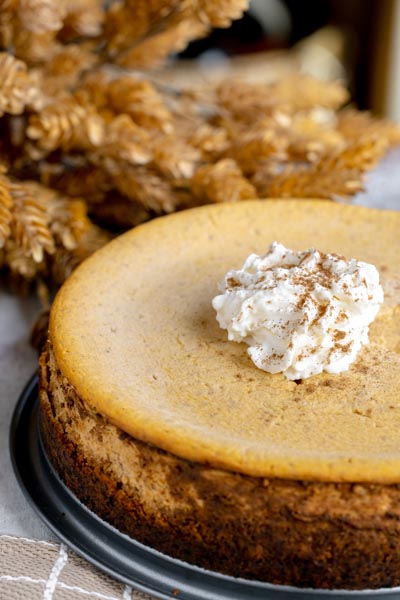 A whole keto pumpkin cheesecake topped with whipped cream and cinnamon, surrounded by autumn leaves.
