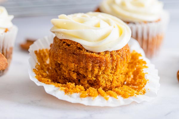 the muffin liner peeled down from a pumpkin muffin that is topped with cream cheese frosting