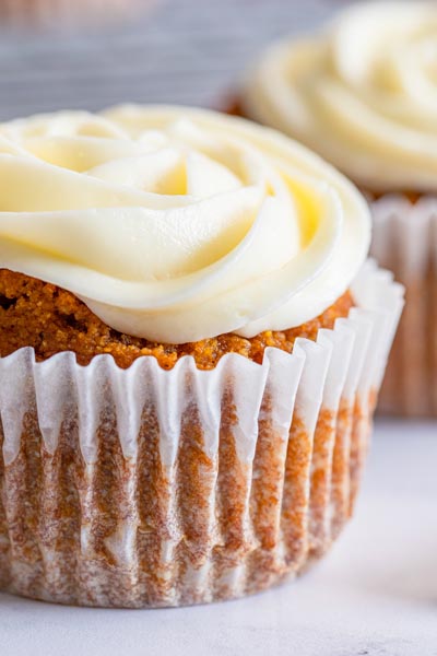 Close up of a pumpkin cupcake topped with creamy cream cheese frosting.