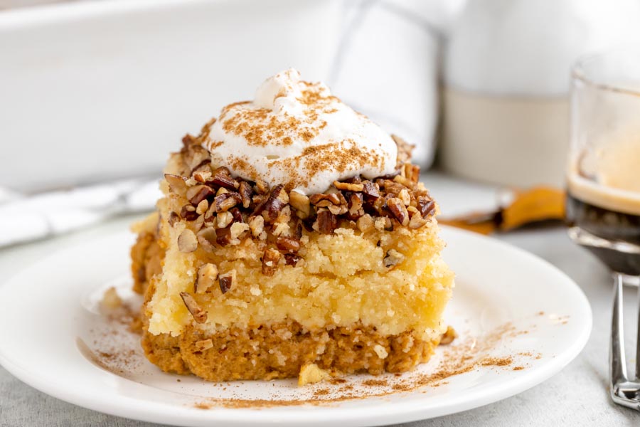 A slice of pumpkin dump cake on a plate topped with crunchy pecans and whipped topping.