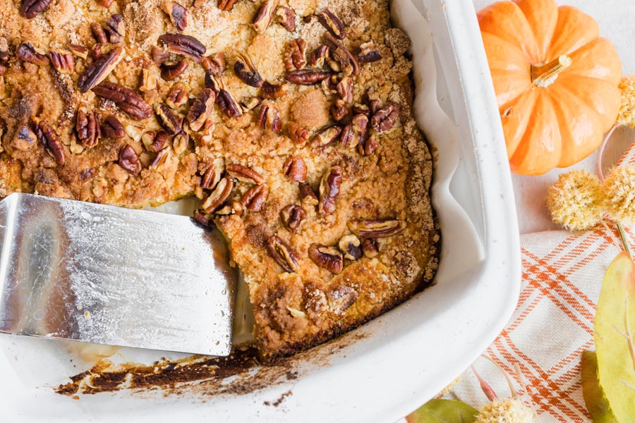 A pecan topped cake in a baking dish with a slice cut out and a spatula scooping up another slice.