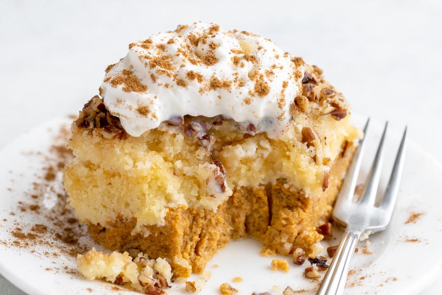 A piece of pumpkin cake on a plate next to a fork with a bite taken out of the cake.