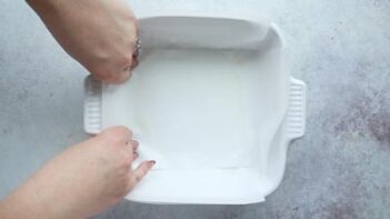 Two hands lining a square baking dish with parchment paper.