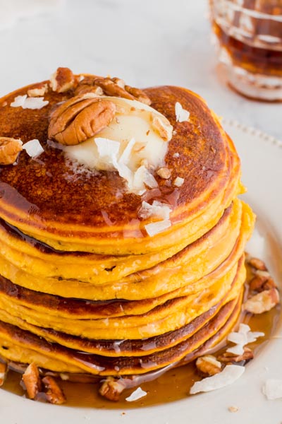 pumpkin pancakes stacked on a plate with pecans, coconut and butter