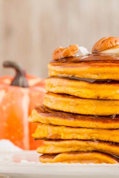 close up of a stack of pumpkin pancake with an orange pumpkin in the backgroun