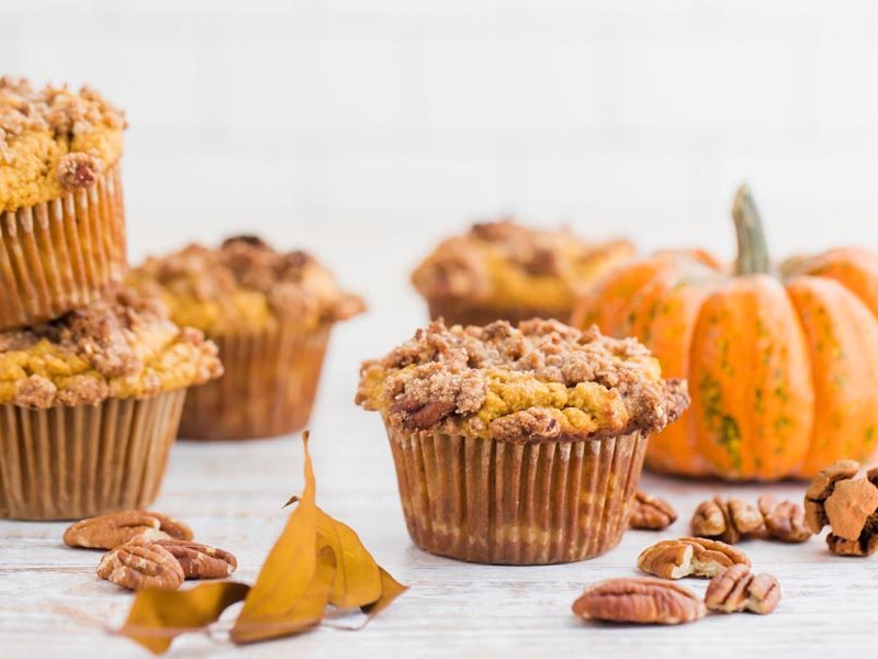 a bunch of pumpkin pecan muffins next to scattered pecans