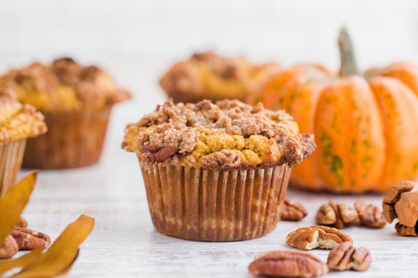 a fluffy pumpkin muffin with streusel topping in front of a pumpkin