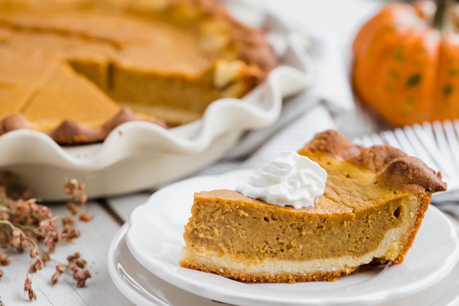 a slice of pumpkin pie on a plate in front of a whole pie on the holiday table