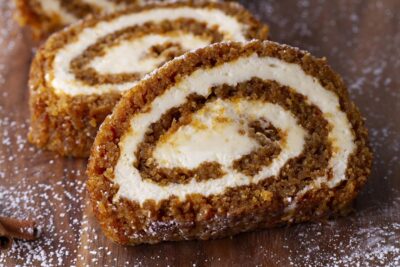 Two slices of pumpkin roll cake on a wooden board, dusted with powdered sweetener.